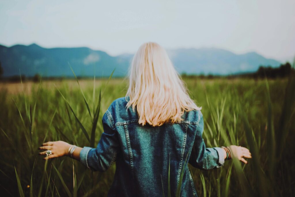 Blonde woman in denim surrounded by lush countryside in Ohlstadt, Germany. Serene and natural.